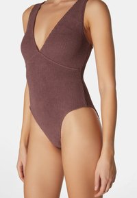 Rippierter einteiliger Badeanzug in staubigem Mauve, mit tiefem V-Ausschnitt, breiten Trägern und hochgeschnittenen Beinausschnitten für eine schlanke Silhouette.