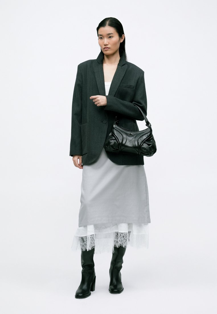 Blazer gris surdimensionné, robe blanche ajustée avec bordure en dentelle, sac à main noir et bottes noires jusqu'aux genoux. Tissu lisse et forme structurée.