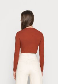 Top cropped de mangas longas na cor ferrugem com textura canelada. Combinado com jeans brancos de cintura alta com bolsos traseiros.