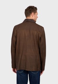 Chaqueta de cuero marrón con cuello de pana, con un corte recto, bolsillos laterales y detalles de costura visibles en la parte posterior.