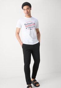 White cotton t-shirt featuring a red and blue graphic print that reads, "Wear the Code," paired with black slim-fit pants and black sandals.