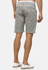 Shorts gris clair avec un motif subtil de palmiers, poignets roulés et poches arrière avec fermeture à bouton. Matériau en coton, design décontracté.