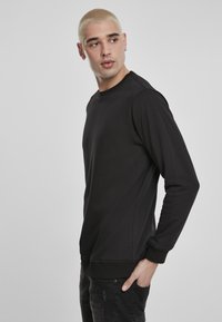 Svart sweatshirt med rund hals, lange ermer og ribbestrikkede mansjetter. Glatt tekstur, minimalistisk design uten synlige mønstre.