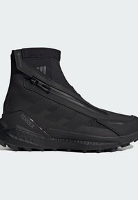 Baskets montantes noires avec un dessus en synthétique lisse, fermeture éclair, semelle texturée et accents de marque. Conçues pour la performance en extérieur.