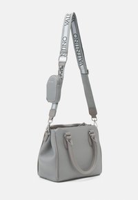 Bolso de piel gris con dos asas, una correa ajustable que presenta el texto "Valentino" y un pequeño pouch desmontable. Cierre con cremallera.