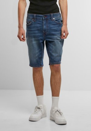 Denim shorts in een middenblauwe wassing, met een klassiek vijf-pocket ontwerp, gestikte accenten en een relaxte pasvorm, gecombineerd met witte sneakers.