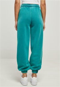 Teal fleecebukser med elastisk liv, avsmalnede mansjetter og sidelommer. Kombinert med hvite joggesko. Minimalistisk design.