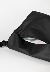 Schwarze Stofftasche mit glatter Textur und Reißverschlussöffnung, ausgestattet mit einem gemusterten Innenfutter und verstellbarem Tragegurt.