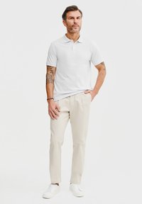 Biała koszulka polo, kremowe spodnie i białe sneakersy. Posiada krótkie rękawy i klasyczny kołnierzyk. Prosta, gładka tkanina bez wzorów.