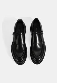 Black leather shoes with a smooth finish, featuring double buckle hardware and a rounded toe design. Textured sole and insoles visible.