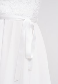 Vit klänning med spetstopp, ett flödande satin kjol och ett satinbälte knutet i midjan, som framhäver mjuk textur och sömlös design.