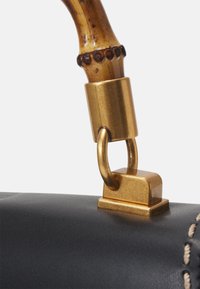 Sort læderhåndtaske med en guldfarvet lås, et bambusgreb og kontrastsyninger, der fremhæver dens strukturerede overflade og elegante design.