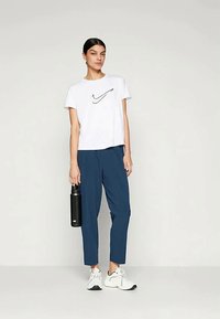 White cotton t-shirt with black Nike logo, paired with navy blue tapered pants, holding a black water bottle, and wearing white sneakers.