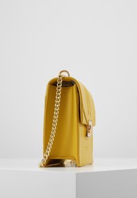 Gelbe Lederhandtasche mit strukturiertem Finish, goldener Kettenriemen und gesichertem Klappenverschluss. Einfacher geometrischer Stil und schlankes Design.