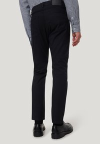 Schwarze Slim-Fit-Hosen mit glatter Textur und Five-Pocket-Design, kombiniert mit schwarzen Schuhen. Der Stoff wirkt robust und vielseitig.
