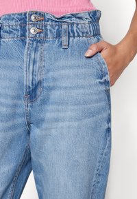 Vaaleansiniset farkut, joissa on hieman haalistunut viimeistely, korkea vyötärö, kaksi etutaskua ja kaksi napin suljinta ylhäällä.