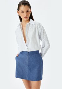 Gestreiftes Button-Up-Hemd in Weiß und Hellblau mit dekorativen Perlenverzierungen, kombiniert mit einem strukturierten blauen Minirock mit Taschen.