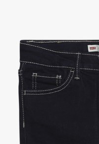 Jeans de mezclilla oscura con costuras blancas visibles, diseño de cinco bolsillos y una pequeña etiqueta de Levi's adjunta a la cintura.
