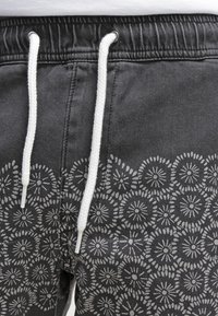 Black shorts made of cotton with a drawstring waistband, featuring a contrasting gray floral pattern along the lower edge.