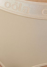 Beige ondergoed met een geribbelde textuur. De brede tailleband heeft een reliëf merknaam in een lichtere kleur, wat zorgt voor een goede, comfortabele pasvorm.