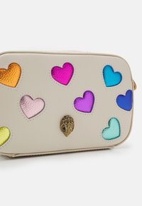 Béžová obdélníková taška s různými barevnými výřezy srdíček. Má texturovaný povrch a akcenty ze zlaceného kovu.