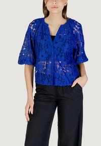Blusa in pizzo di un blu brillante con motivi floreali, maniche corte e scollatura rotonda, abbinata a pantaloni neri con vestibilità morbida.