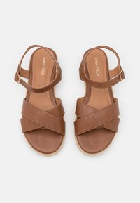 Brown faux leather sandals with crisscross straps, adjustable ankle strap, and woven jute-style sole. Smooth texture and simple design.
