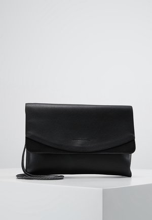 Bolso de mano de cuero negro con solapa plegable y correa de cadena plateada, apoyado sobre una superficie blanca contra un fondo liso.