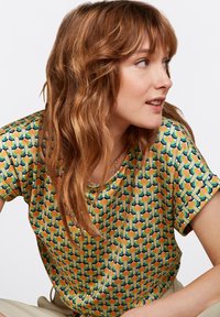 Lyhythihainen T-paita, jossa on kukkakuosi oranssilla, vihreällä ja sinisellä keltaisella taustalla. Valmistettu pehmeästä kankaasta ja rento istuvuus.