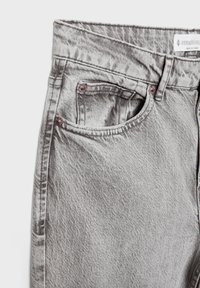 Sive traperice s visokim strukom, dizajn od pet džepova i suptilna tekstura. Sadrže metalne detalje u suptilnoj nijansi i kontrastnu špagu.