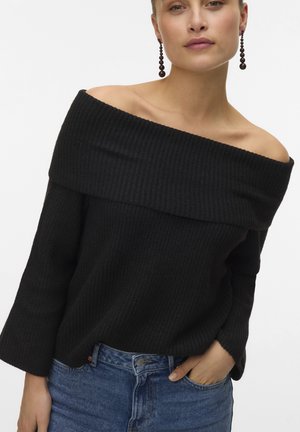 Maglione a maniche lunghe nero a spalle scoperte, in tessuto a coste; fabbricazione testurizzata, vestibilità rilassata. Abbinato a jeans in denim blu. Design semplice.