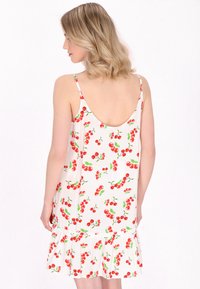 Abito bianco senza maniche con stampa di ciliegie in rosso e verde. Il design include un bordo arricciato e una schiena bassa.