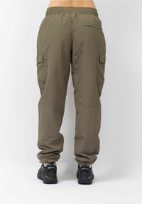 Olijfgroene cargobroek met elastische tailleband, twee zijzakken en een lichte, gestructureerde stof, gecombineerd met zwarte buitenschoenen.