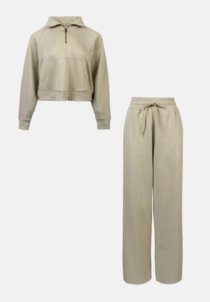 Haut à capuche beige court avec demi-fermeture éclair, poche avant et poignets côtelés, associé à un pantalon large à cordon de serrage assorti. Texture lisse.