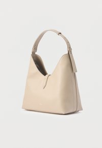 Μπεζ δερμάτινη τσάντα ώμου με έναν ρυθμιζόμενο ιμάντα, ελάχιστη ραφή και μικρό χρυσό λογότυπο στο κάτω κέντρο της μπροστινής πλευράς.
