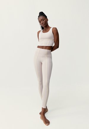 Ljust beige träningsset som består av en kort tanktopp och högmidjade leggings med gula sömmar. Slät textur, figurnära design.