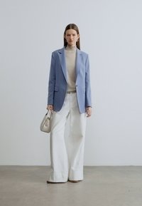 Ανοιχτό μπλε σακάκι, μπεζ ζιβάγκο και λευκός παντελόνι με φαρδύ πόδι. Αξεσουάρ περιλαμβάνουν μια μικρή κρεμ τσάντα. Λείο ύφασμα με μοντέρνο σχέδιο.