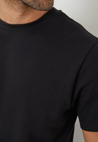 Camiseta negra de canalé con cuello redondo y mangas cortas. La tela tiene una textura suave con sutiles rayas verticales.