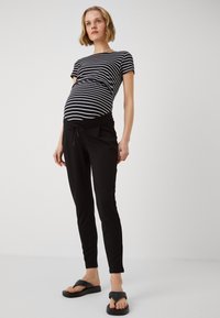 Svart gravid joggebukser med snøring i midjen, kombinert med en svart og hvit stripet tettsittende topp. Glatt stoff med en avslappet passform.