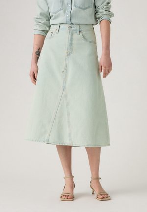 Hellblauer Denim-Midirock mit Frontnaht-Detail, getragen zu einem passenden langärmligen Denimhemd und beigen Riemchen-Sandaletten mit Absatz.