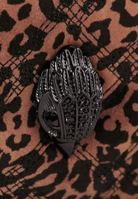 Tissu à imprimé léopard avec un suède marron doux, orné d'une garniture noire texturée et brillante avec des accents de pierres précieuses.