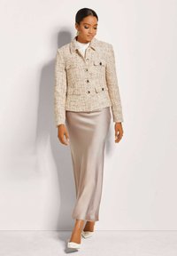 Tweedjasje met een kraag en dubbelknopen, gecombineerd met een lange satijnen rok in een zachte beige tint en witte hakken.