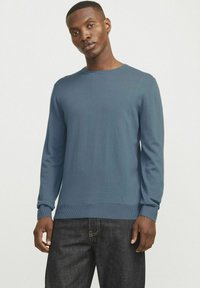 Blauer Langarmpullover aus glattem Strickstoff, mit rundem Halsausschnitt und gerippten Bündchen und Saum, getragen mit dunklen Jeans.