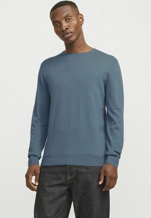 Suéter azul de manga larga en un tejido de punto suave, con un escote redondeado y puños y dobladillo acanalados, combinado con pantalones oscuros.