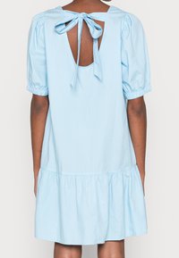 Světle modré bavlněné šaty s nabíranými rukávy, s volánkovou sukní a zavazováním na zádech. Obsahují nabírané detaily na rukávech a lemu.