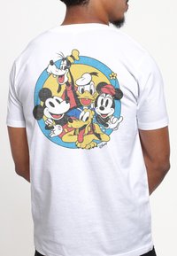Vit bomull t-shirt med en färgglad tecknad tryck av Mickey Mouse, Kalle Anka, Långben, Pluto och Musse Pigg inom en blå cirkel.