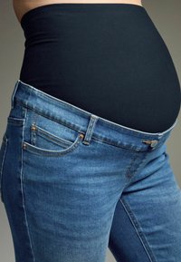 Jeans de maternidad con una textura de denim azul claro, que presentan una cinturilla negra elástica y un diseño clásico de cinco bolsillos.