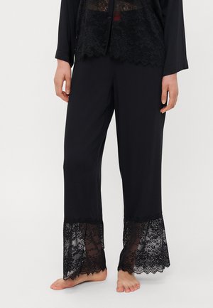 Zwarte broek met doorschijnende kantaccenten aan de zoom. Zachte stof met een losse pasvorm, met fijne kantafwerking langs de onderrand.
