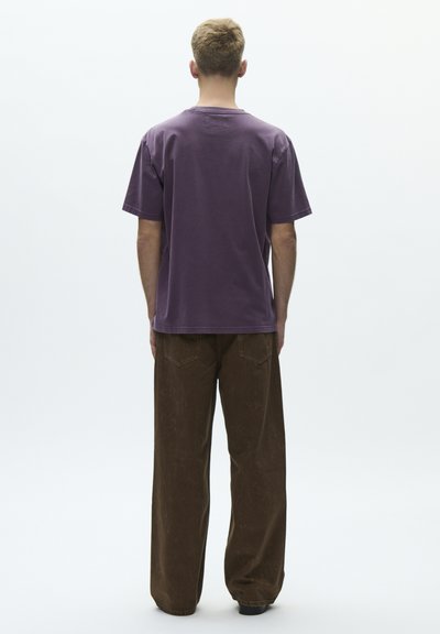 Lilla bomulls-t-skjorte med avslappet passform og korte ermer, kombinert med brune vidbukser med baklommer og en falmet tekstur.
