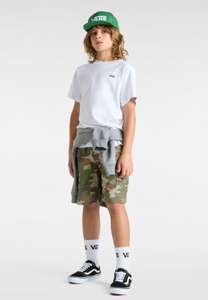 Camiseta blanca de manga corta con el logo negro de Vans, pantalones cortos de camuflaje, sudadera gris atada a la cintura, zapatos negros de Vans y gorra verde.